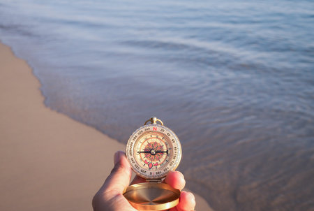 Close up hand holding compass with beach background in the sunset time