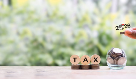 Hand putting coin into glass bottle and wooden block with word TAX on stack of coins. The concept of...