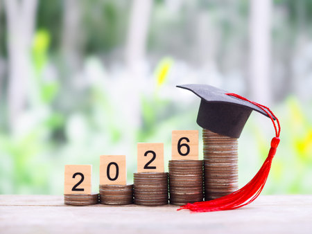 Wooden blocks with the number 2026 and stack of coins with graduation hat. The concept of saving...