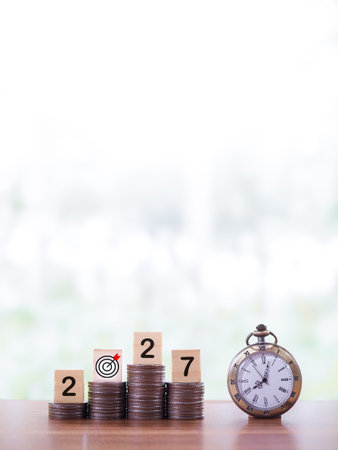 Vintage watch, Wooden blocks with the number 2027 on stack of coins. The concept of saving money for...