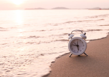 White alarm clock on the beach in the sunset time. The concept about Time to summer, Travel, Vacation and Relaxationの写真素材