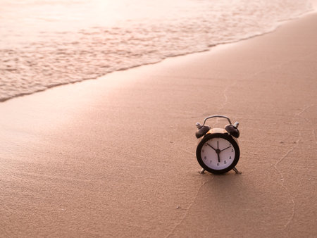 Black alarm clock on the beach in the sunset time. The concept about Time to summer, Travel,...