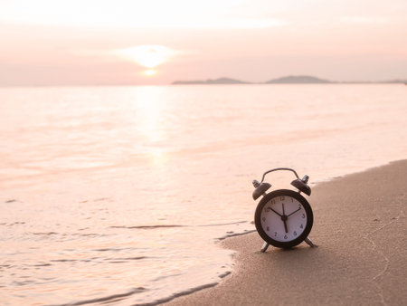 Black alarm clock on the beach in the sunset time. The concept about Time to summer, Travel,...
