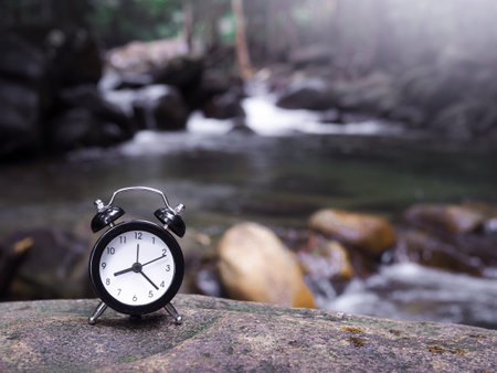 Black alarm clock on the rock with stream as background. The concept of world tourism day, Searching...