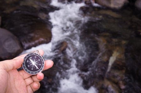 Close up of compass in woman hand with waterfall as background. The concept of world tourism day,...