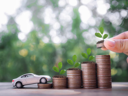 Close up hand putting coin in stack of coins with Toy car. The concept of saving money and manage to success transport businessの写真素材