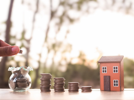 Hand putting coin into glass bottle, Miniature house and stack of coins. The concept of saving money for house, Property investment, House mortgage, Real estate in the futureの写真素材