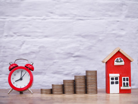 Miniature house, Read alarm clock and stack of coins. The concept of saving money and and manage time for house, Property investment, House mortgage, Real estate in the futureの写真素材