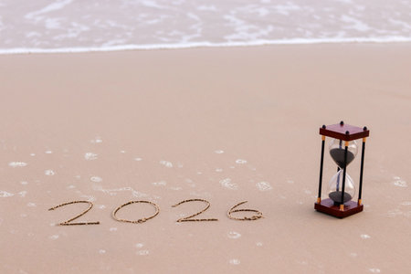 Handwritten inscription 2026 on the beach in the sunset time with hourglass. The concept of...
