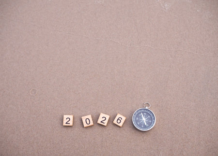 Wooden blocks with the number 2026 and Compass on beach sand background. The concept of world...