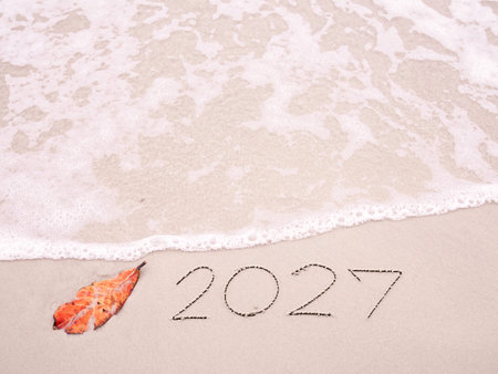 2027 year handwritten with ocean waves on a sandy beach. New Year 2027 concept