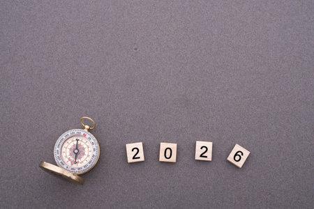 Wooden blocks with the number 2026 and Compass on beach sand background. The concept of world...