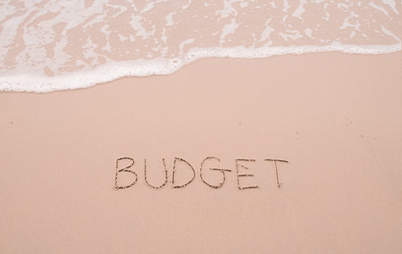 BUDGET handwritten with ocean waves on a sandy beach. The concept about budget planning and...