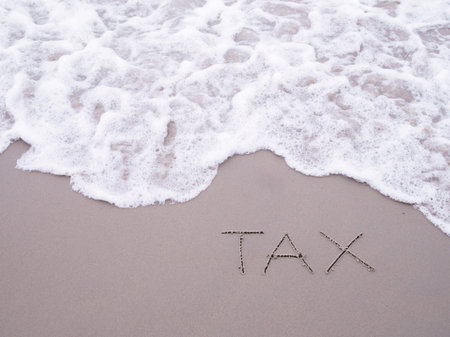 TAX handwritten with ocean waves on a sandy beach.の写真素材