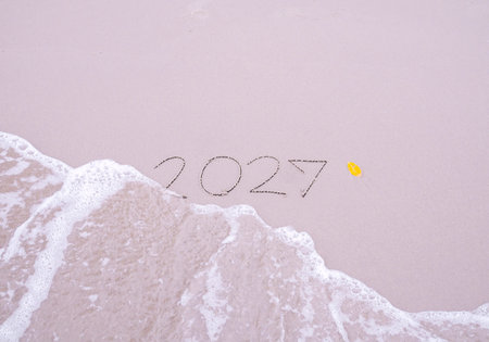 2027 year handwritten with ocean waves on a sandy beach. New Year 2027 concept