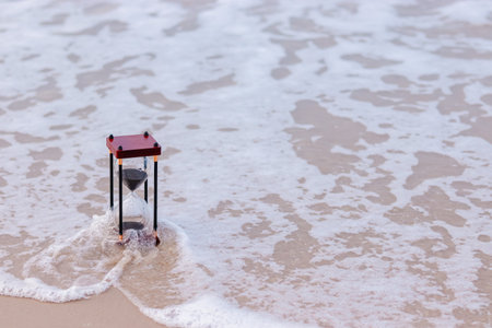 Hourglass on the beach with ocean waves. The concept about countdown to Summer, Travel, Vacation and Relaxation.の写真素材