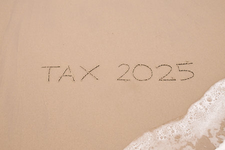 TAX 2025 handwritten with ocean waves on a sandy beach.の写真素材