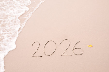 2026 year handwritten with ocean waves on a sandy beach. New Year 2026 concept