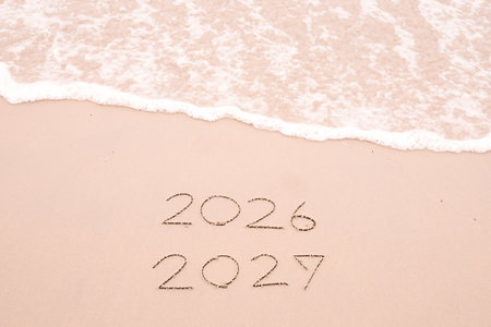 Handwritten inscription 2026 and 2027 with ocean waves on a sandy beach. The concept of Goodbye 2026 and Happy New Year 2027の写真素材