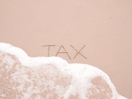 TAX handwritten with ocean waves on a sandy beach.の写真素材