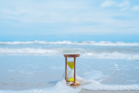 Hourglass on the beach with ocean waves. The concept about countdown to Summer, Travel, Vacation and Relaxation.の写真素材