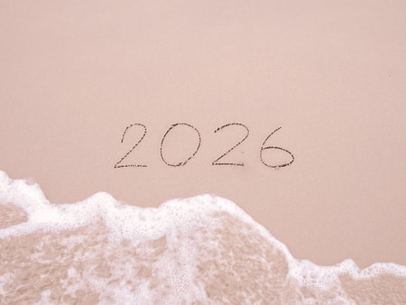 2026 year handwritten with ocean waves on a sandy beach. New Year 2026 concept