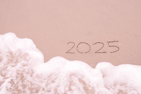 2025 year handwritten with ocean waves on a sandy beach. New Year 2025 conceptの写真素材