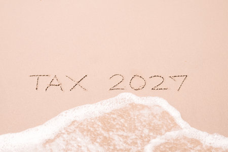 TAX 2027 handwritten with ocean waves on a sandy beach.の写真素材