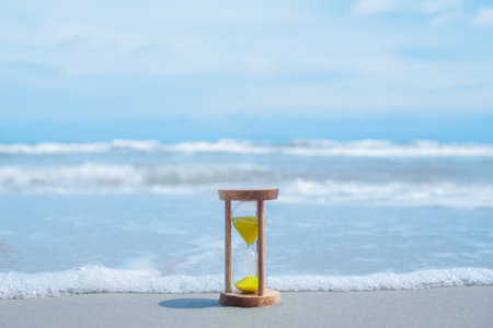 Hourglass on the beach with ocean waves. The concept about countdown to Summer, Travel, Vacation and Relaxation.の写真素材