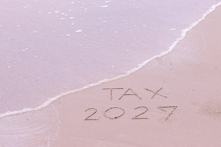 TAX 2027 handwritten with ocean waves on a sandy beach.