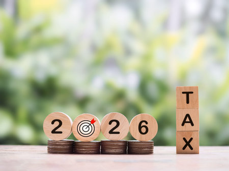 Wooden blocks with the word TAX and Number 2026 on stack of coins. The concept about saving money to...