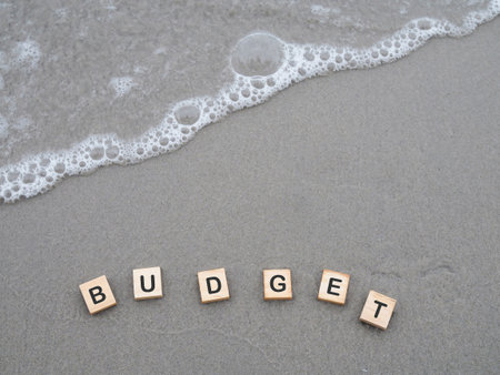 Wooden blocks with the word BUDGET on the beach with ocean waves. The concept about budget planning and allocationの写真素材