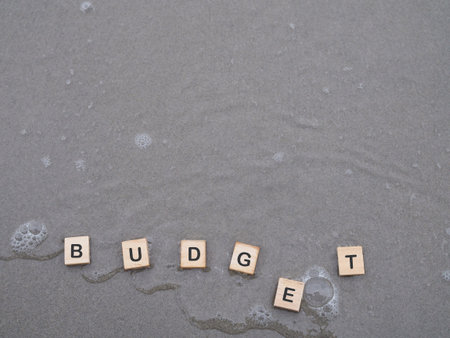 Wooden blocks with the word BUDGET on the beach with ocean waves. The concept about budget planning...