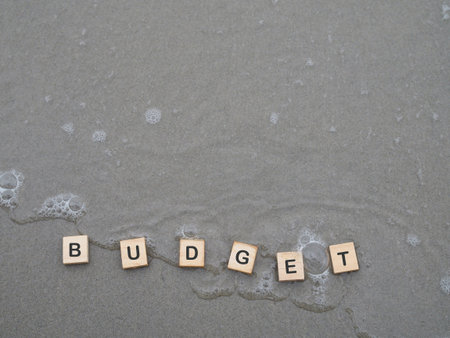 Wooden blocks with the word BUDGET on the beach with ocean waves. The concept about budget planning and allocationの写真素材