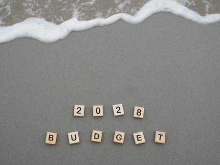 Wooden blocks with the word 2028 BUDGET on the beach with ocean waves. The concept about budget planning and allocation in year 2028の写真素材