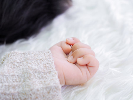Close up of newborn baby hand is wearing a grey sweater on white rugsの写真素材