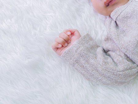 Close up of newborn baby hand is wearing a grey sweater on white rugsの写真素材