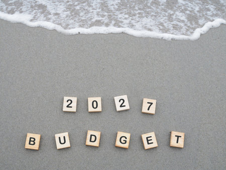 Wooden blocks with the word 2027 BUDGET on the beach with ocean waves. The concept about budget planning and allocation in year 2027の写真素材