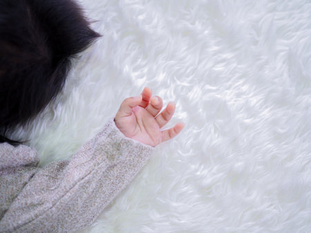 Close up of newborn baby hand is wearing a grey sweater on white rugsの写真素材