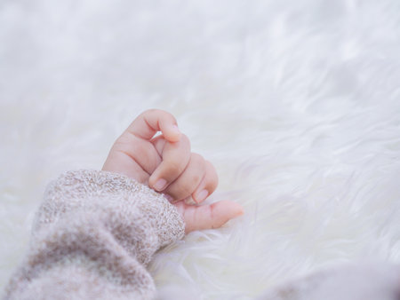 Close up of newborn baby hand is wearing a grey sweater on white rugsの写真素材