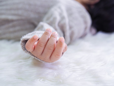 Close up of newborn baby hand is wearing a grey sweater on white rugsの写真素材