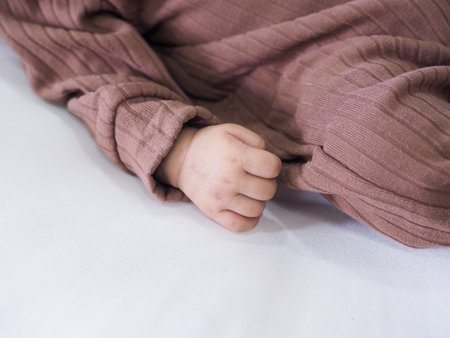 Close up of newborn baby hand is wearing a brown clothes on white bedの写真素材
