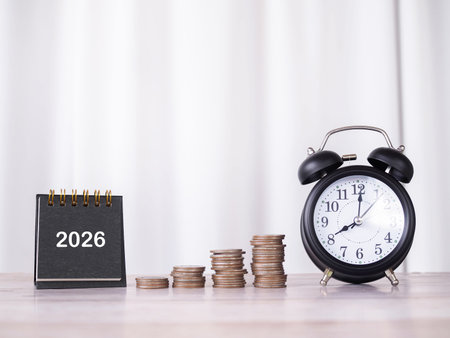 2026 desk calendar, Black alarm and stack of coins. The concept of saving money and manage time for...