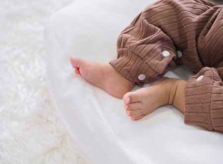 Close up of newborn baby feet is wearing a brown clothes on white bedの写真素材