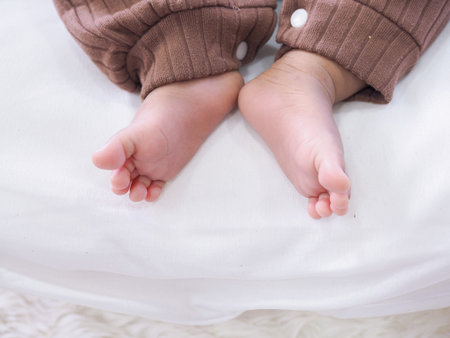 Close up of newborn baby feet is wearing a brown clothes on white bed