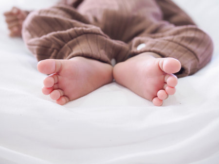 Close up of newborn baby feet is wearing a brown clothes on white bedの写真素材