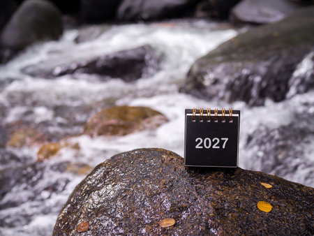 2027 desk calendar on the rock with waterfall as background. Resolution, Goal, Action, Planning, and manage to success business.の写真素材
