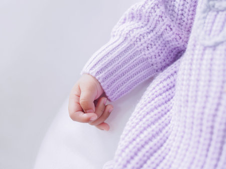 Close up of newborn baby hand is wearing a purple clothes on white bedの写真素材