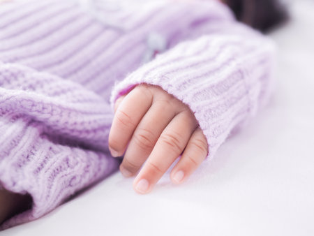 Close up of newborn baby hand is wearing a purple clothes on white bedの写真素材