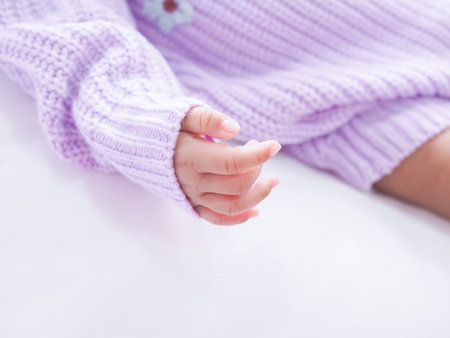 Close up of newborn baby hand is wearing a purple clothes on white bedの写真素材